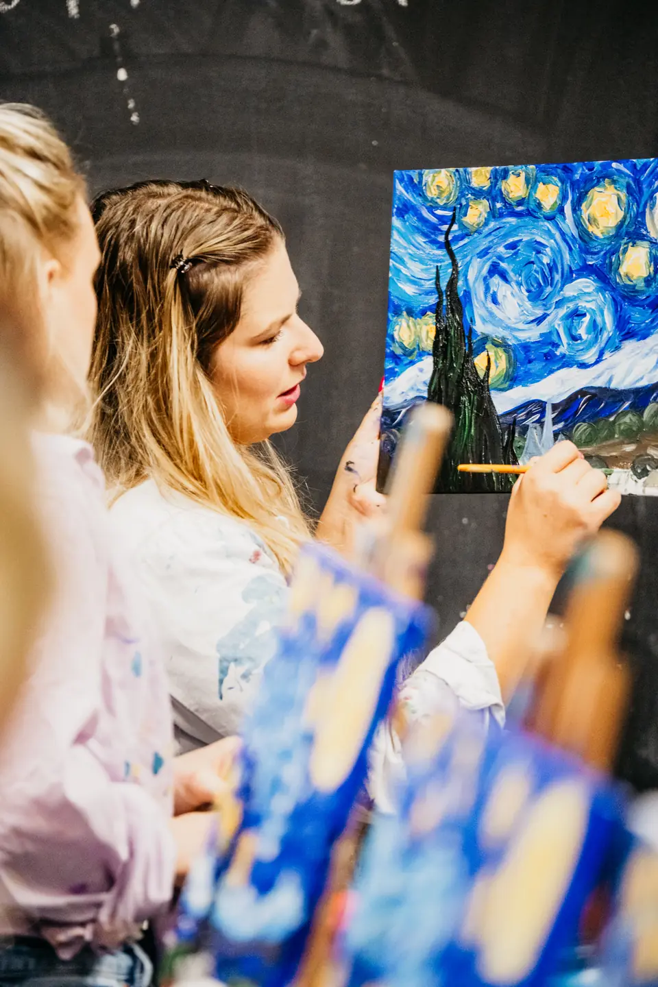 Žena maľuje Hviezdnu noc, v pozadí tabuľa s nápisom @kukkultura